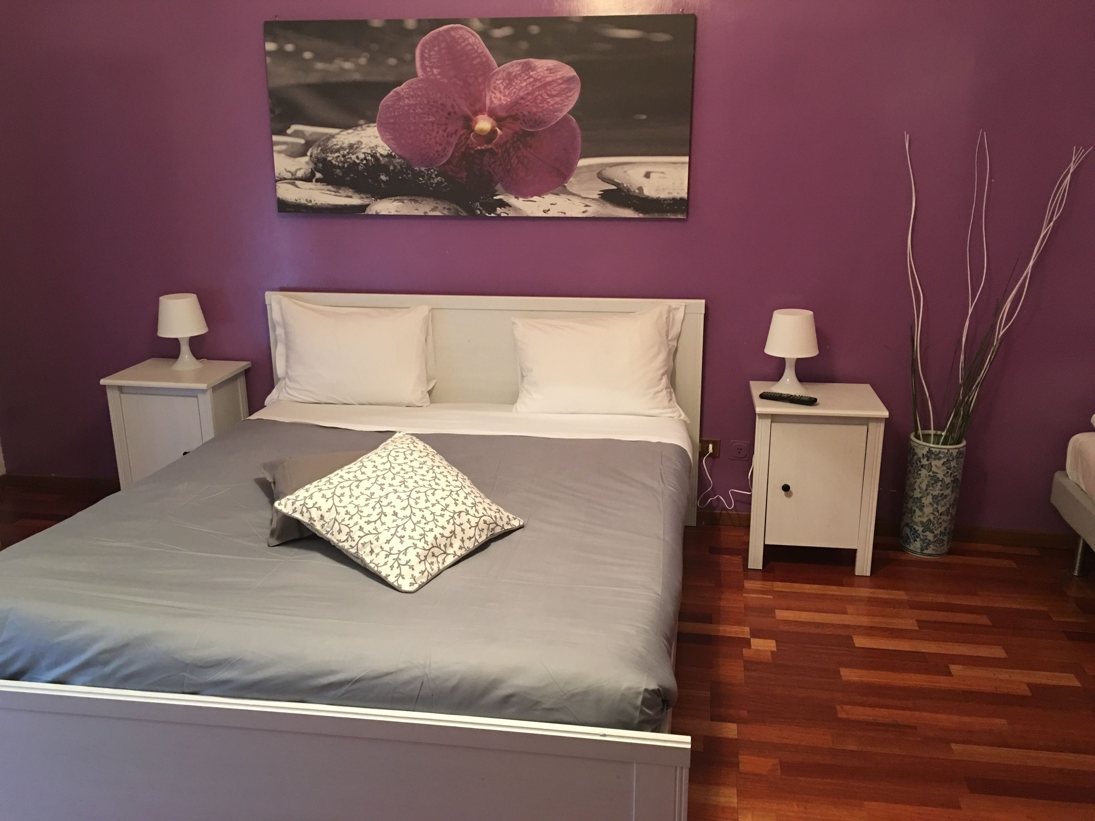 A bedroom with a bed, two nightstands, a vase with branches, and a painting of a flower on the wall.