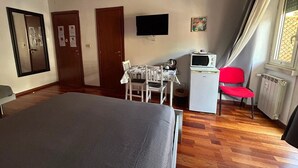 A hotel room with a bed, a desk with a chair, a television, and a window with curtains. - Domum Vaticani (Rome)