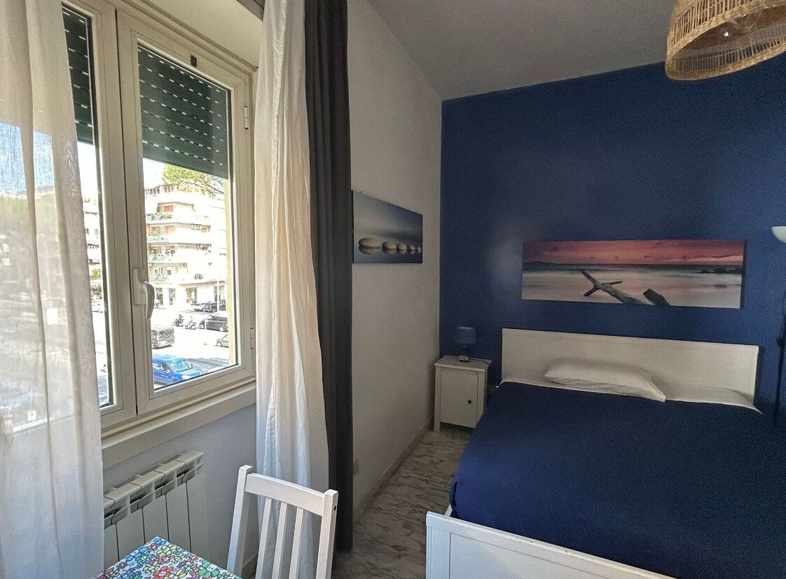 Une chambre à coucher comprenant un lit, une table de chevet, une fenêtre avec des rideaux, un radiateur et une vue sur l’extérieur.