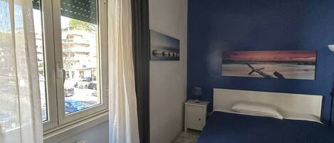 Een slaapkamer met een bed, een nachtkastje, een raam met gordijnen, een radiator en uitzicht.