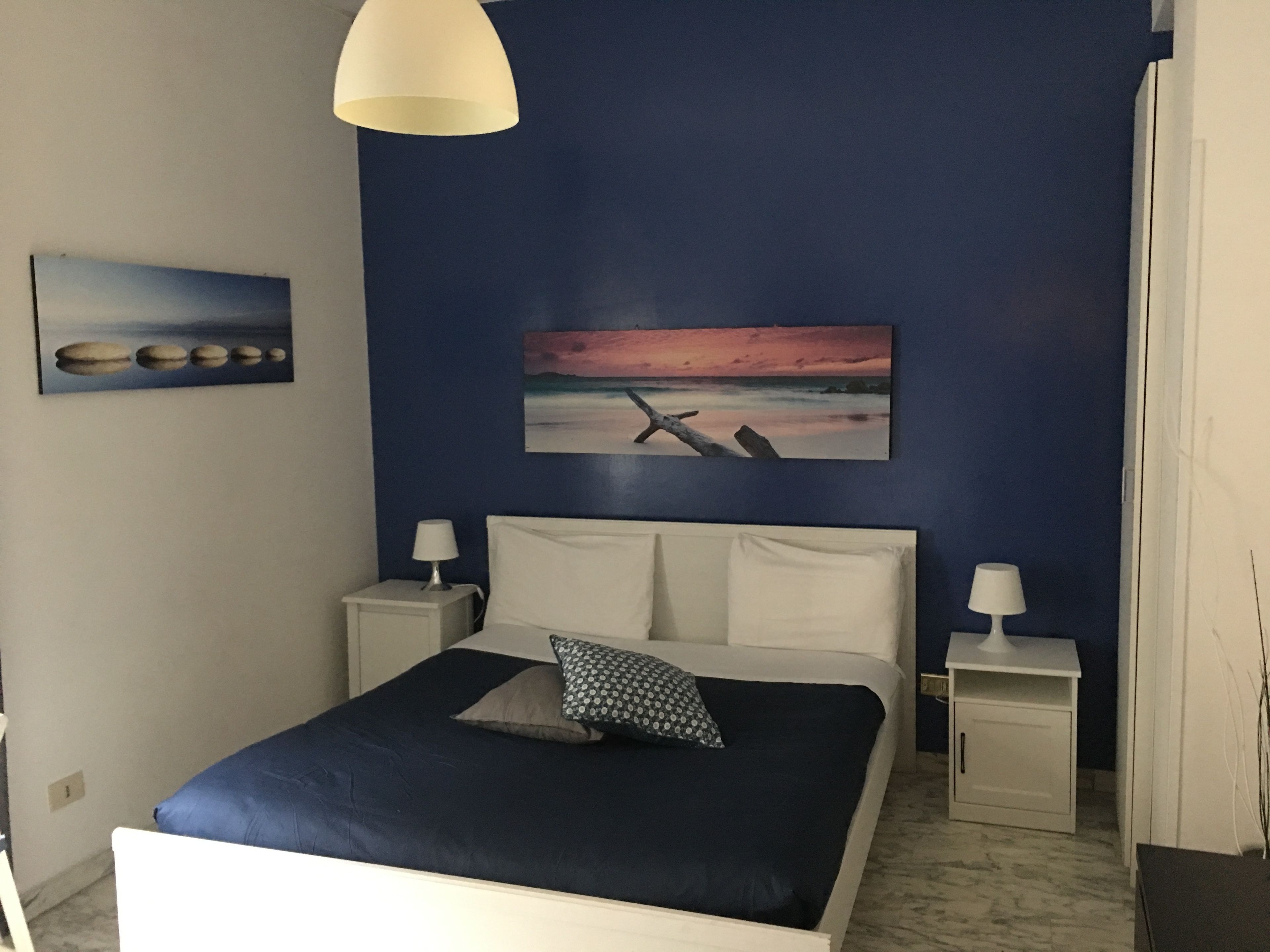 Un dormitorio con una cama, dos mesitas de noche, una lámpara y un cuadro en la pared.