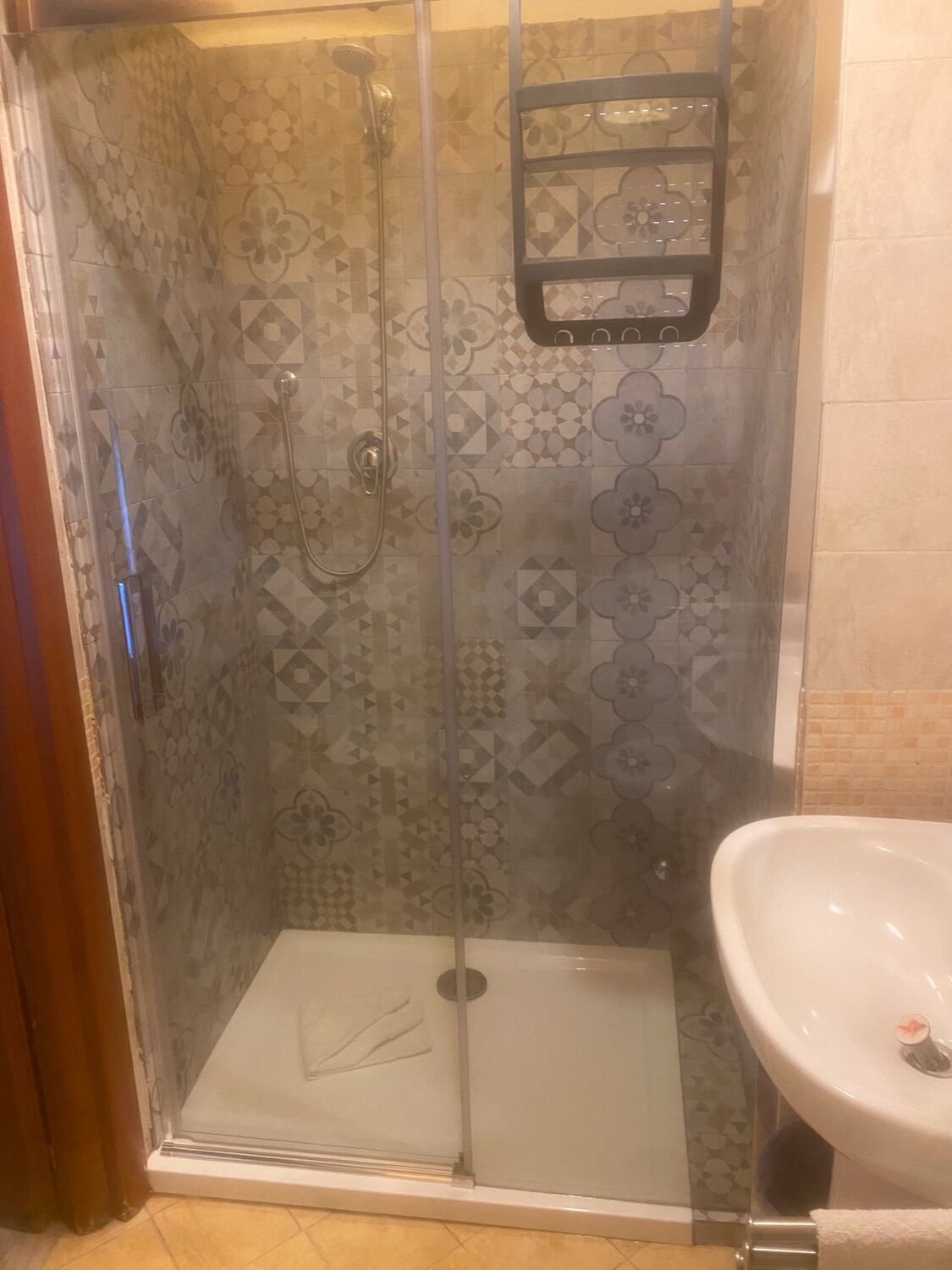 A glass-enclosed shower with a handheld showerhead and a wall-mounted faucet.