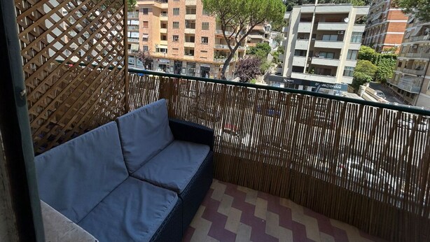 A balcony with a cushioned seating area, a bamboo fence, and a view of multi-story buildings. - Domum Vaticani (Rome)