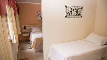 A small, clean room with two beds, a wooden headboard, a decorative wall piece, and a window with curtains.