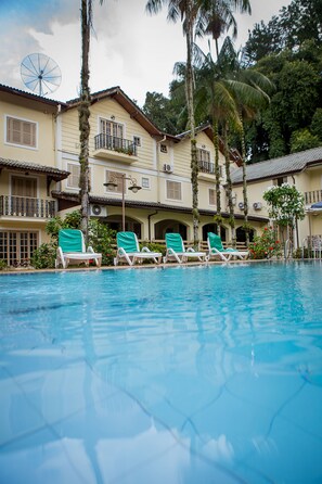 A pool area with lounge chairs and a building with multiple balconies. - Hotel Rio Penedo (Itatiaia)