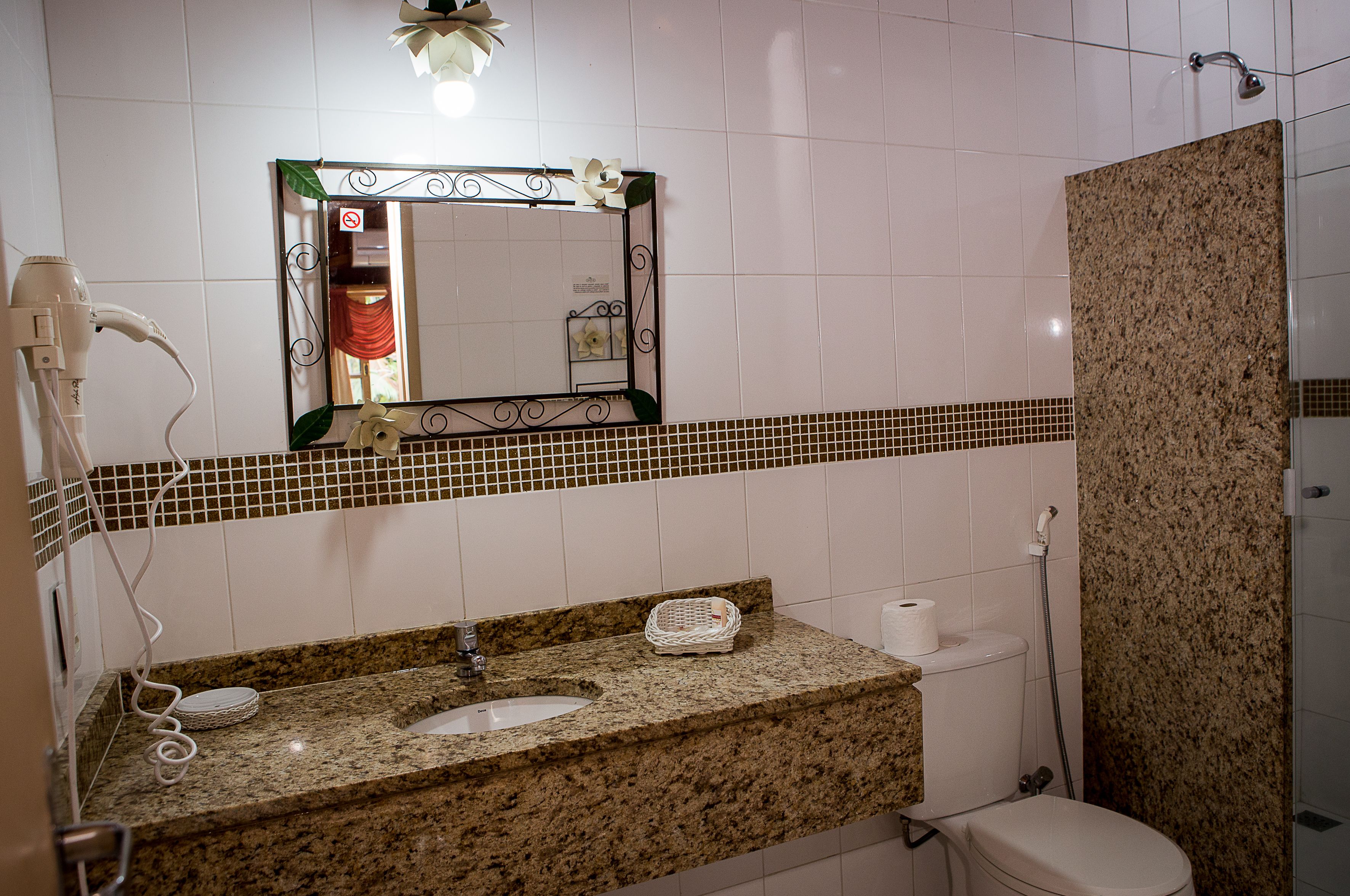 A bathroom with a granite countertop sink, a mirror with a decorative frame, a shower area, and a toilet.