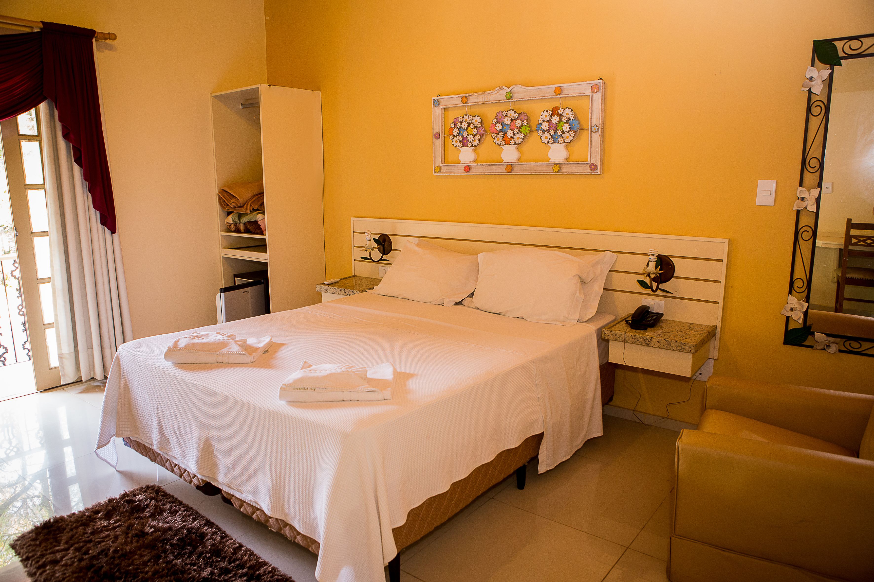 A neatly made bed with white linens and pillows, a bedside table with a phone and a lamp, and a mirror on the wall.