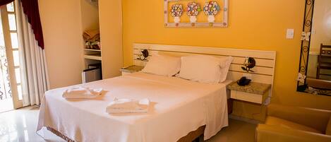 A neatly made bed with white linens and pillows, a bedside table with a phone and a lamp, and a mirror on the wall.