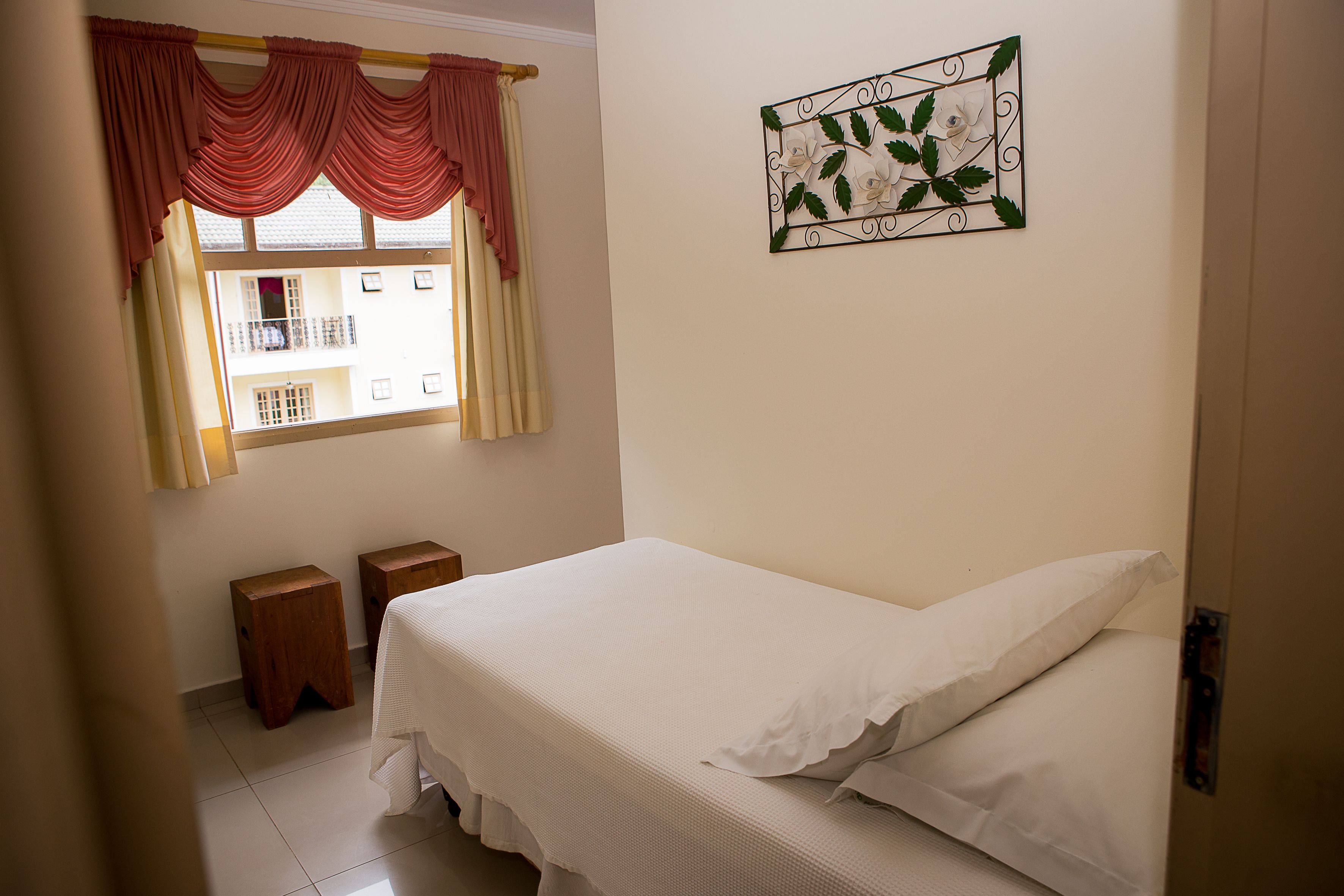 Un dormitorio con cama, dos mesitas de noche, una ventana con cortinas y un adorno en la pared.
