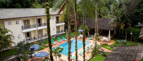 A hotel with a swimming pool, outdoor seating, and lush greenery.