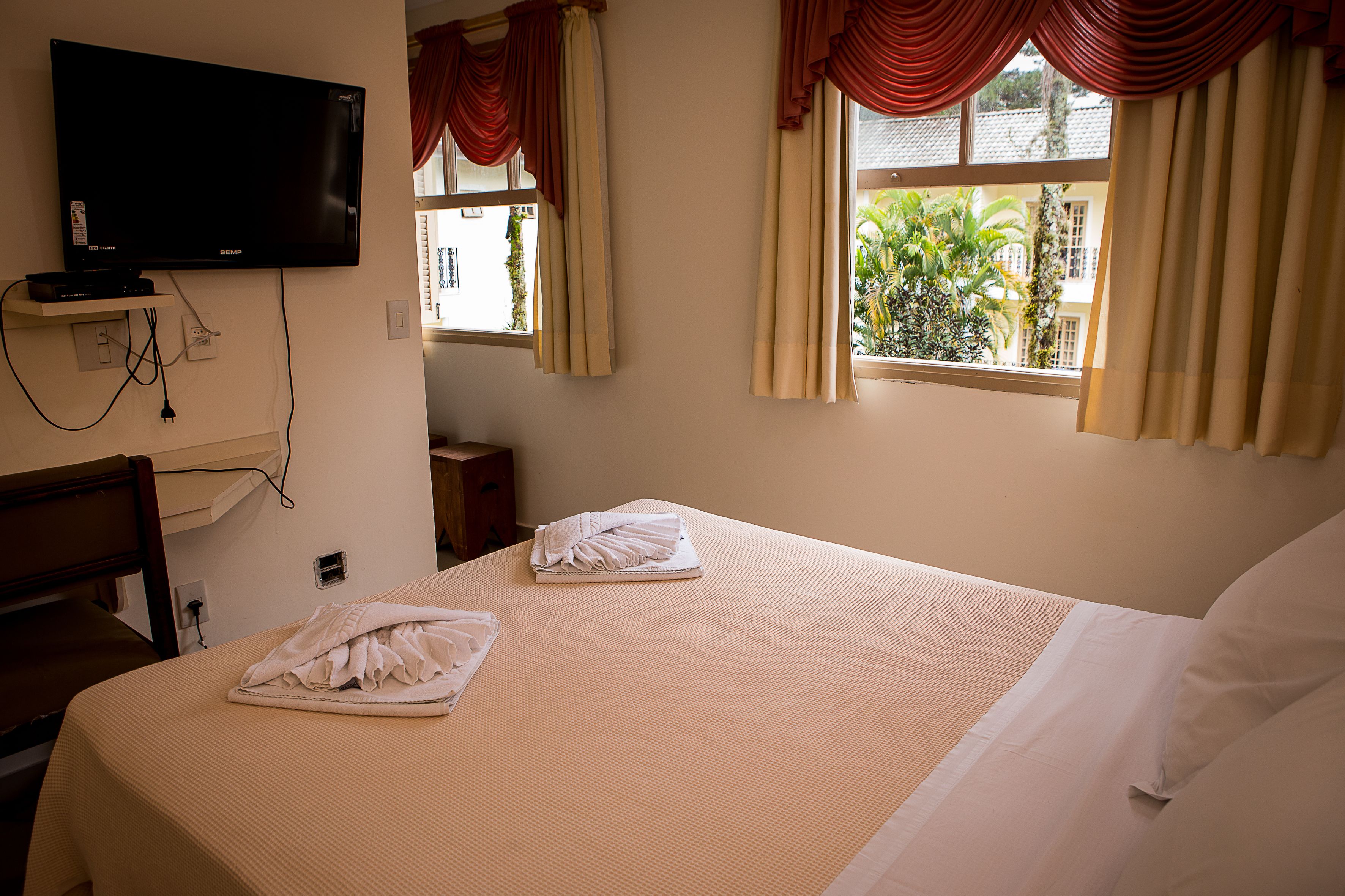 A hotel room with a bed, a TV mounted on the wall, and a window with curtains.