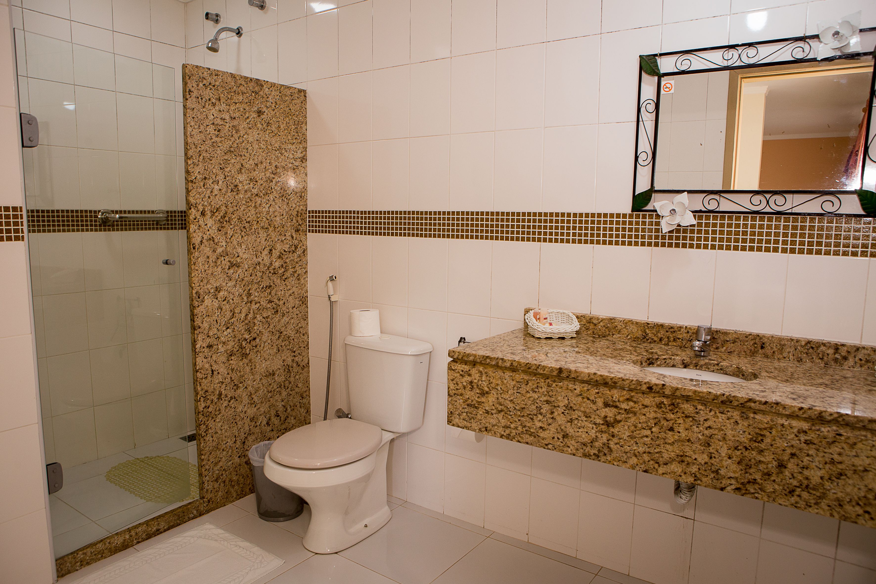 Un baño con ducha, inodoro, lavamanos y espejo con marco decorativo.