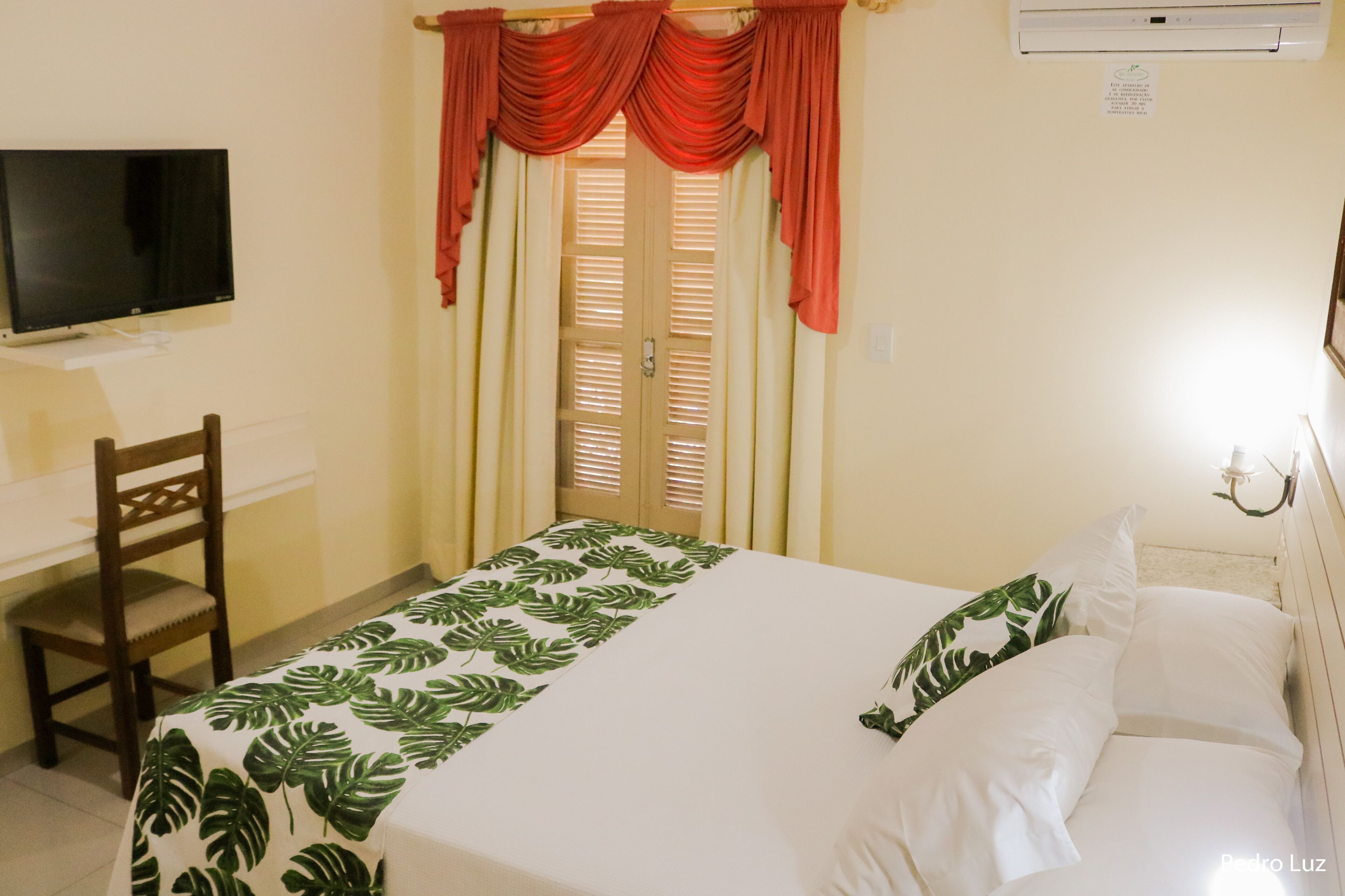 A hotel room with a bed, a desk, a chair, a television, and a window with curtains.