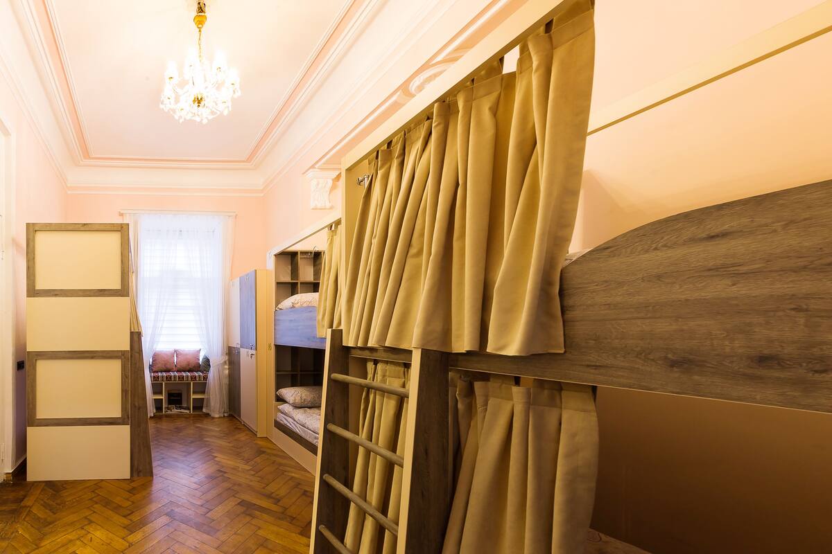 A room with a bunk bed, wooden flooring, a chandelier, and a door leading to another room.