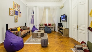 Un salon comprenant un canapé, un fauteuil poire, un pouf et un téléviseur.