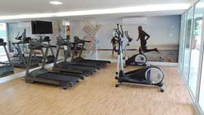 Un gimnasio con cintas de correr, bicicletas estáticas y un espejo grande.
