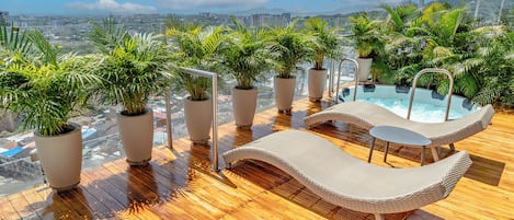 Área de piscina en la azotea con sillas de descanso, plantas en macetas y vistas panorámicas de la ciudad.