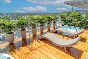 Un espace piscine aménagé sur le toit, avec des chaises longues, des plantes en pot et une vue sur le paysage urbain.