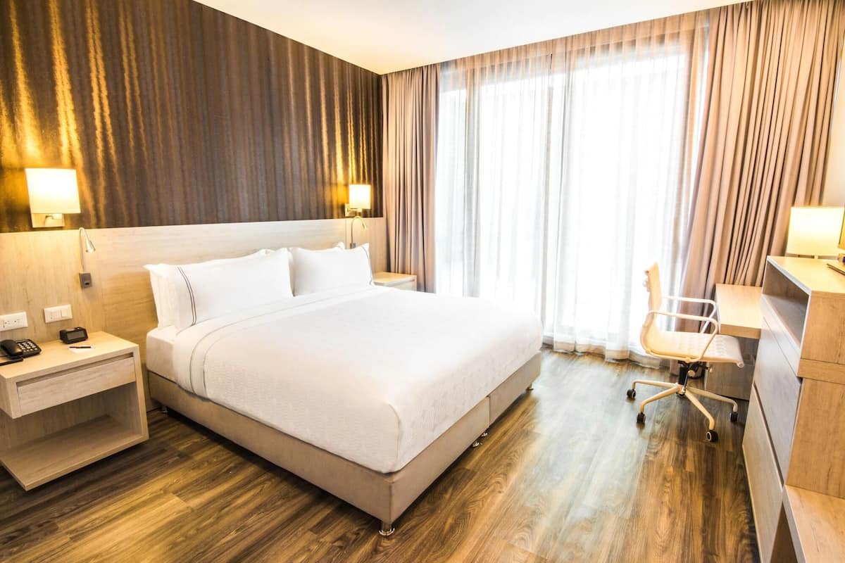Hotelkamer met een bed, nachtkastje, bureau, stoel en groot raam met gordijnen.