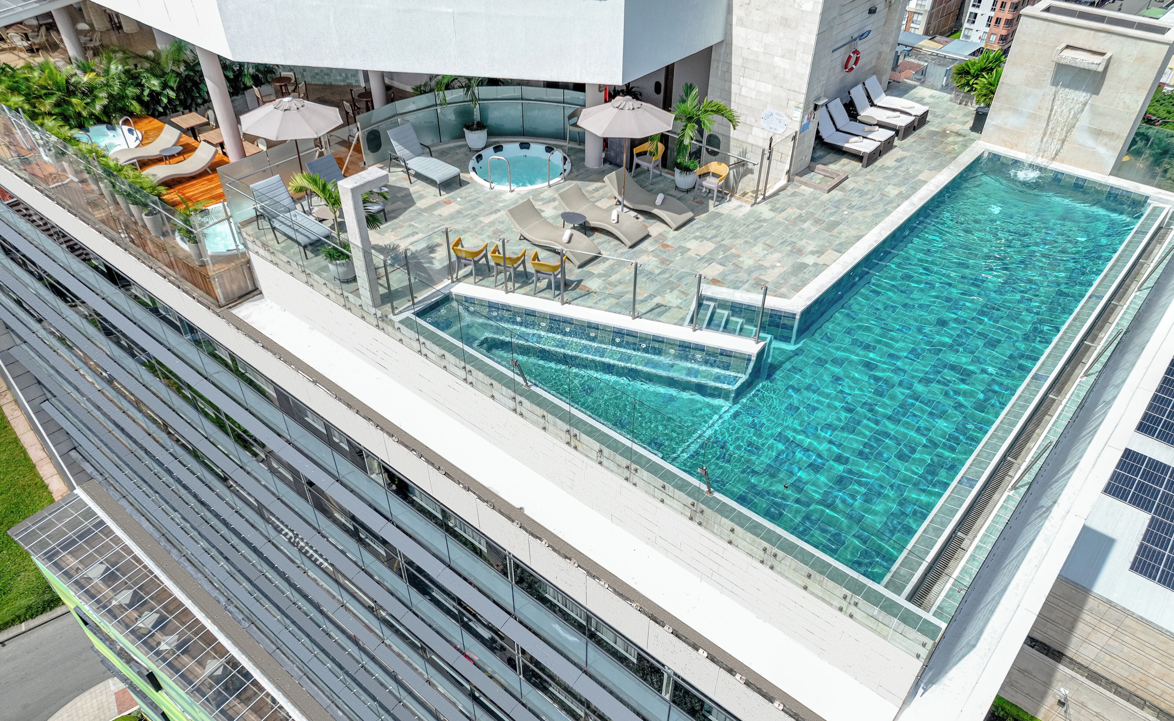 A rooftop pool with sun loungers and umbrellas, surrounded by a glass balustrade.