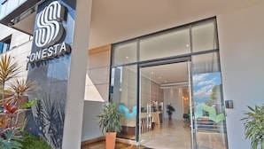 Una entrada de hotel moderna con puerta de vidrio, un logotipo sobre la entrada y plantas en macetas afuera.