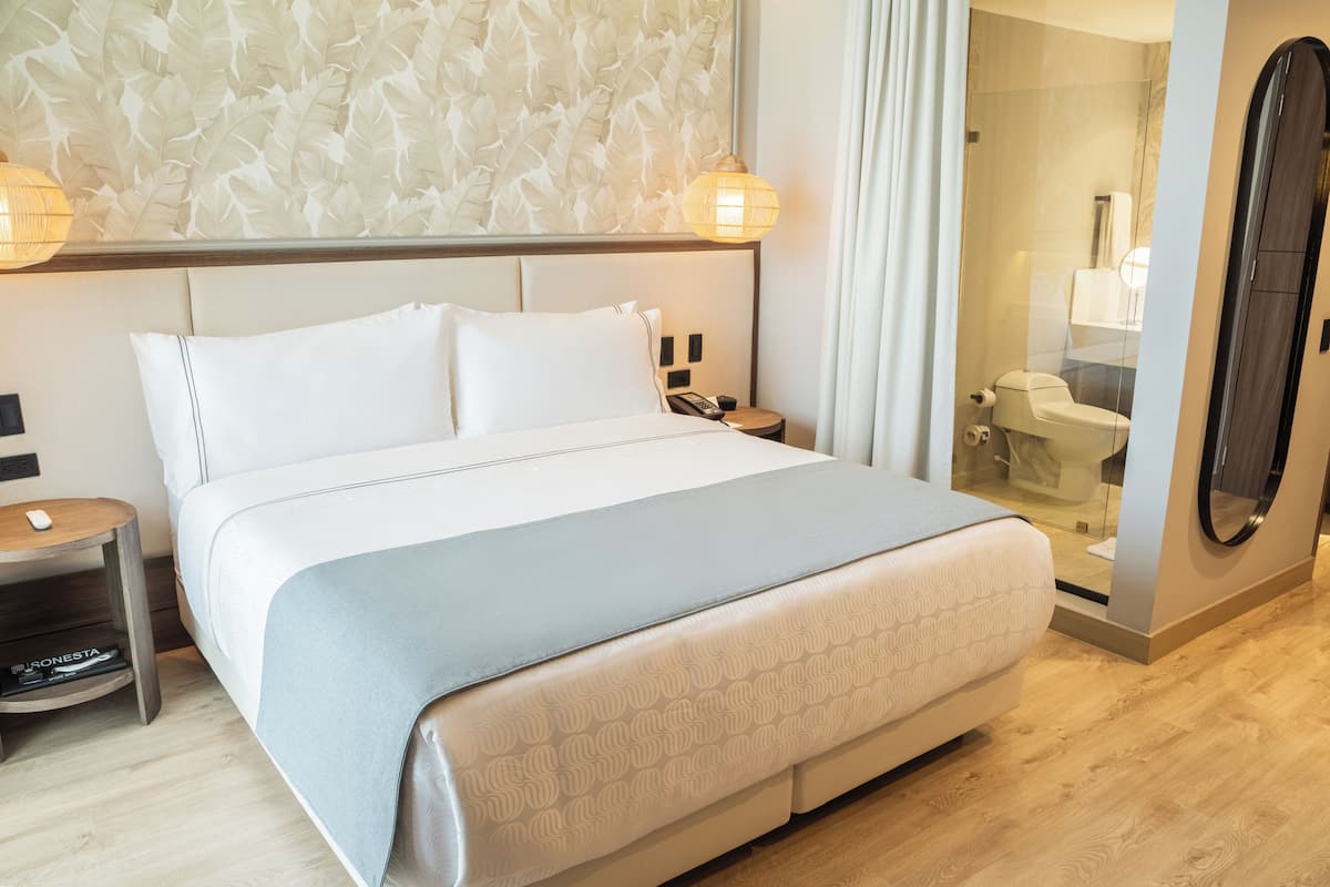 Een hotelkamer met een groot bed, een nachtkastje met een lamp, een spiegel en een douche.