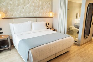 Une chambre d’hôtel avec un grand lit, une table de chevet avec une lampe, un miroir et un espace douche.