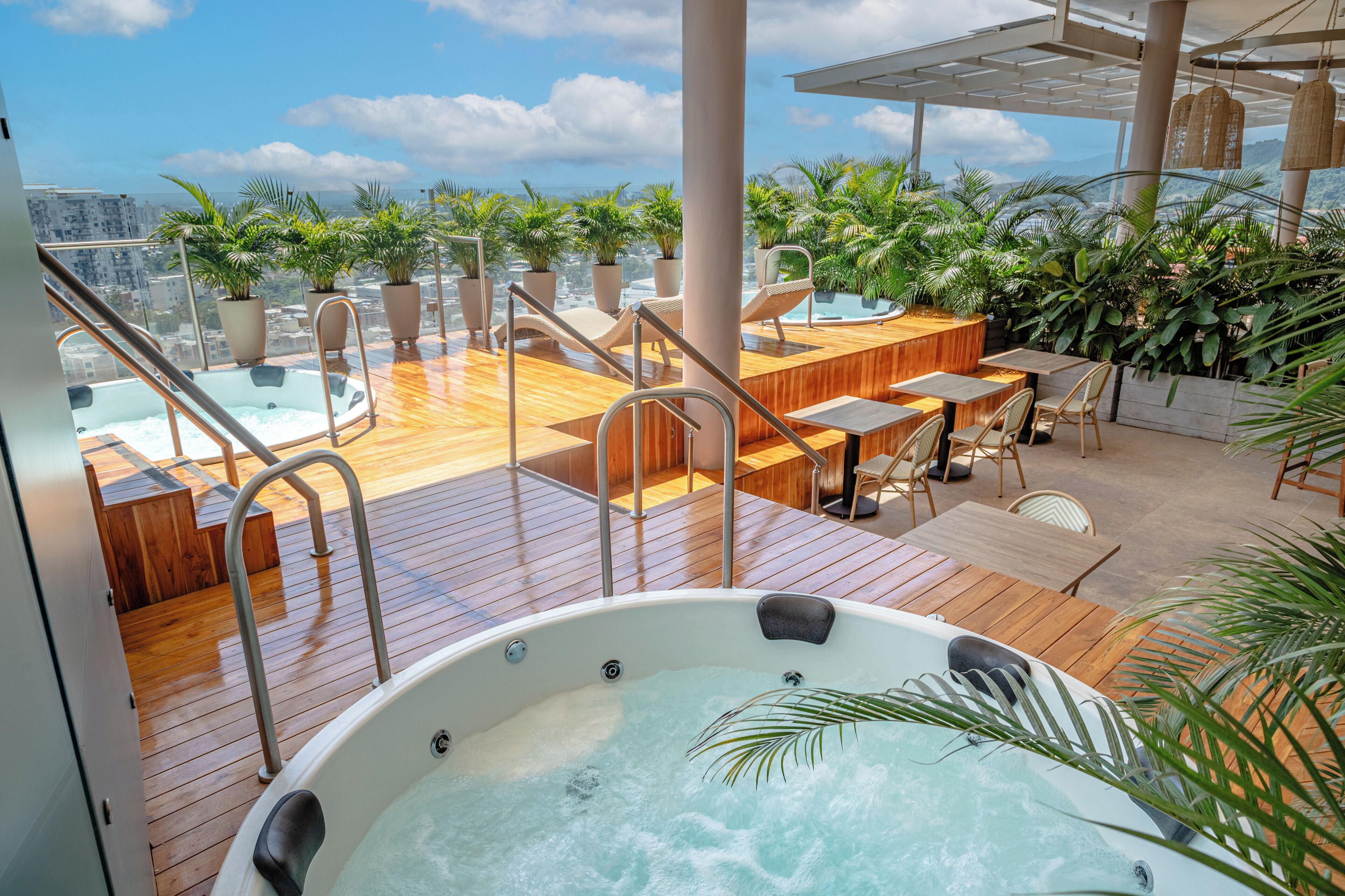A rooftop terrace with a hot tub, wooden deck, outdoor seating, and potted plants.