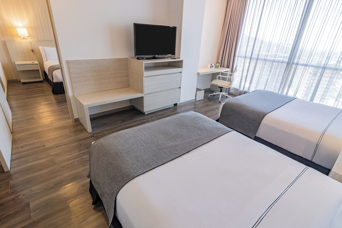 Een moderne hotelkamer met twee bedden, een televisie op een houten standaard, een bureau en een stoel.