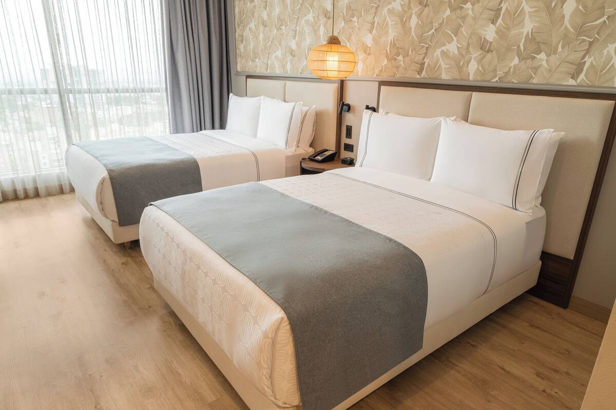 Een hotelkamer met twee bedden, een nachtkastje met een telefoon en een wandlamp.