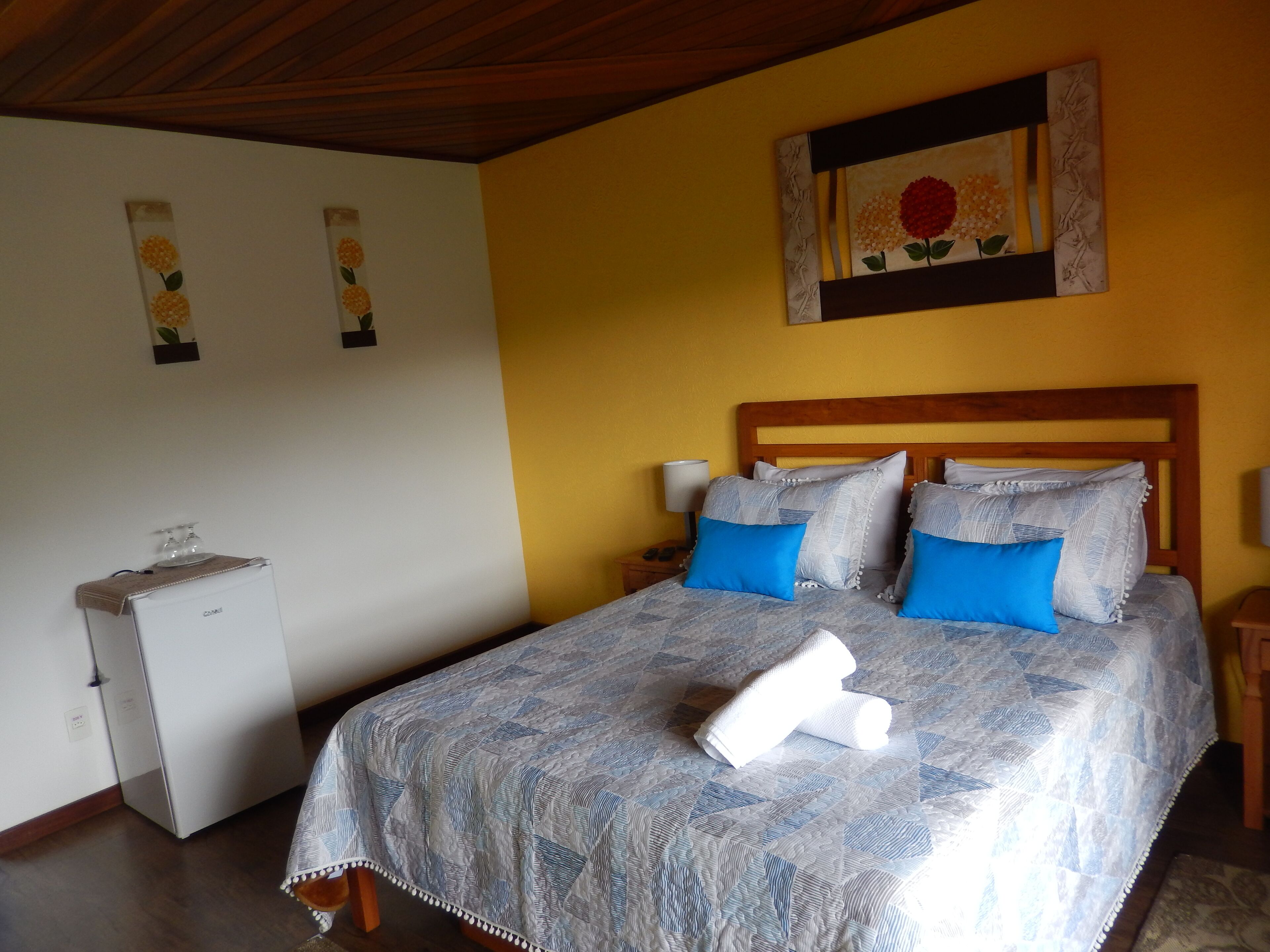 A bedroom with a bed, pillows, a nightstand, a lamp, and a small refrigerator.