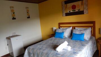 A bedroom with a bed, pillows, a nightstand, a lamp, and a small refrigerator.