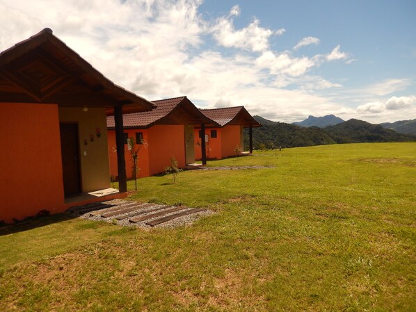 Una hilera de cabañas con techo anaranjado, un campo cubierto de césped y montañas al fondo.