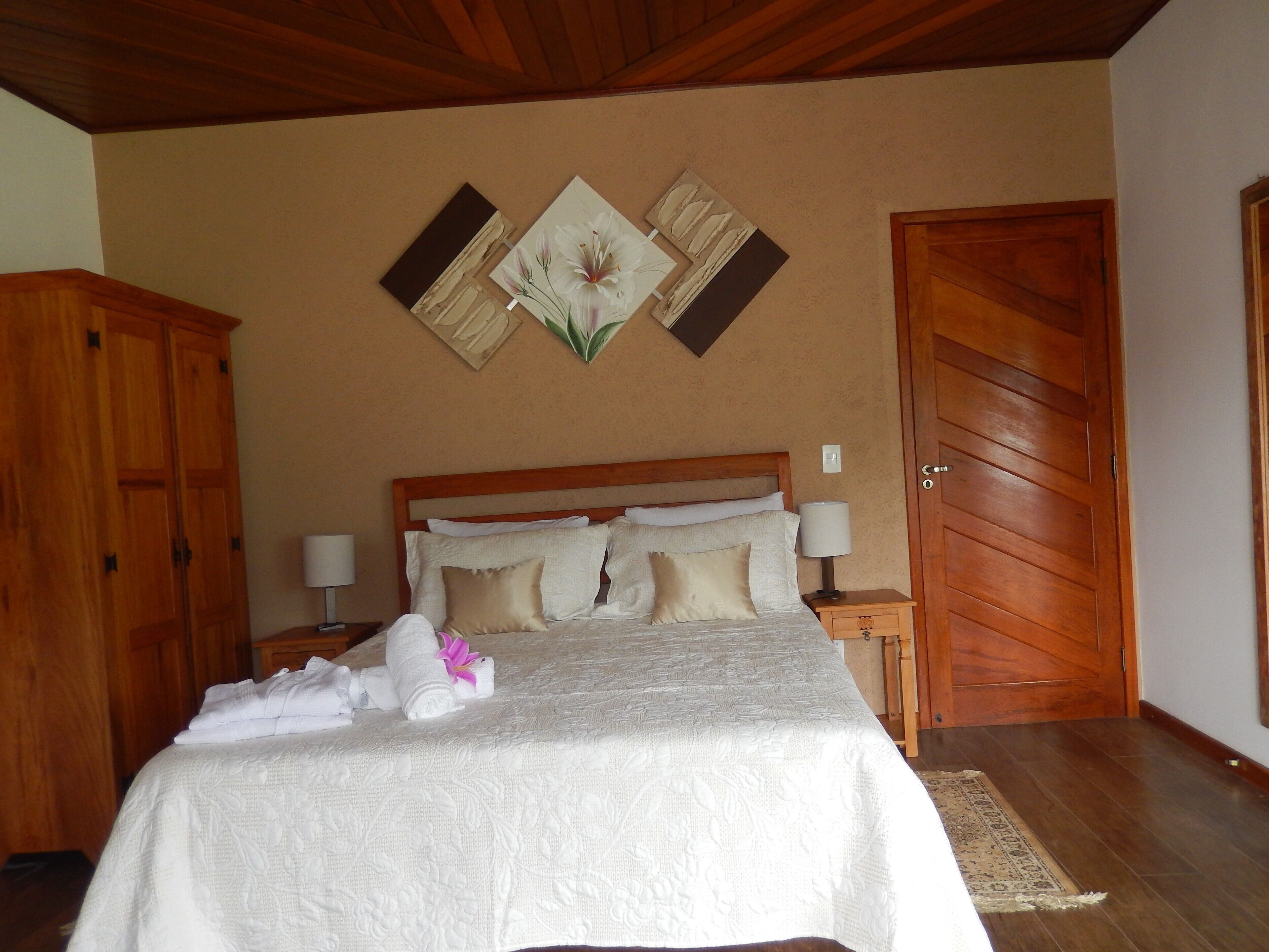 Una cama bien hecha con colcha blanca y almohadas, un cabecero de madera y una mesita de noche con una lámpara.