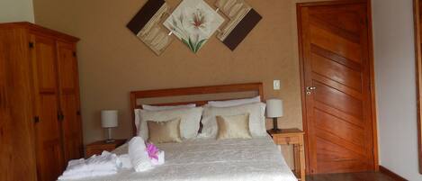 Una cama bien hecha con colcha blanca y almohadas, un cabecero de madera y una mesita de noche con una lámpara.