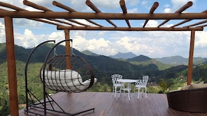 Una pérgola de madera con una silla colgante y una mesa con sillas, con vistas a un paisaje montañoso.