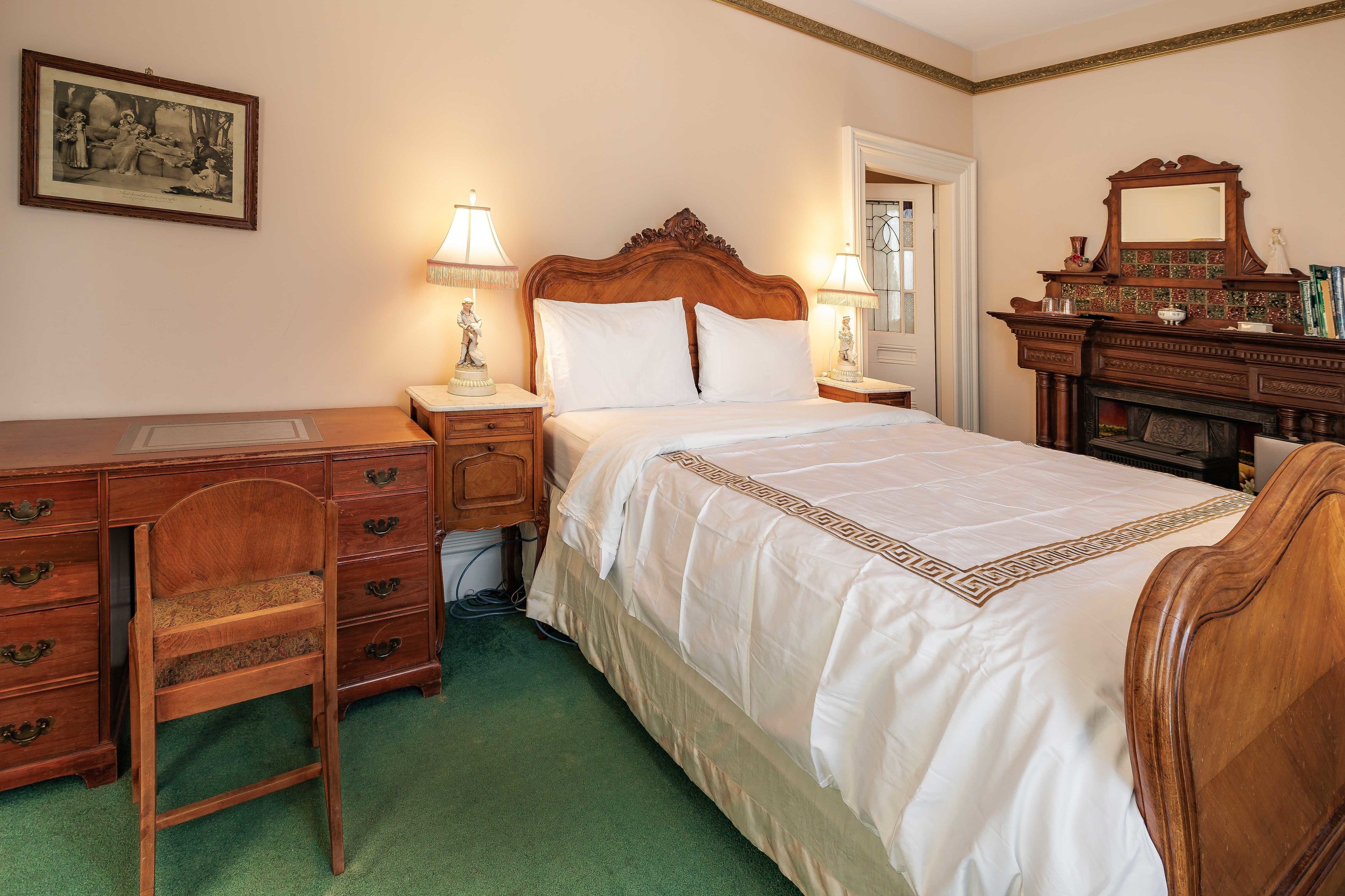 A bedroom with a wooden bed, a desk with drawers, a chair, a dresser, and a mirror.