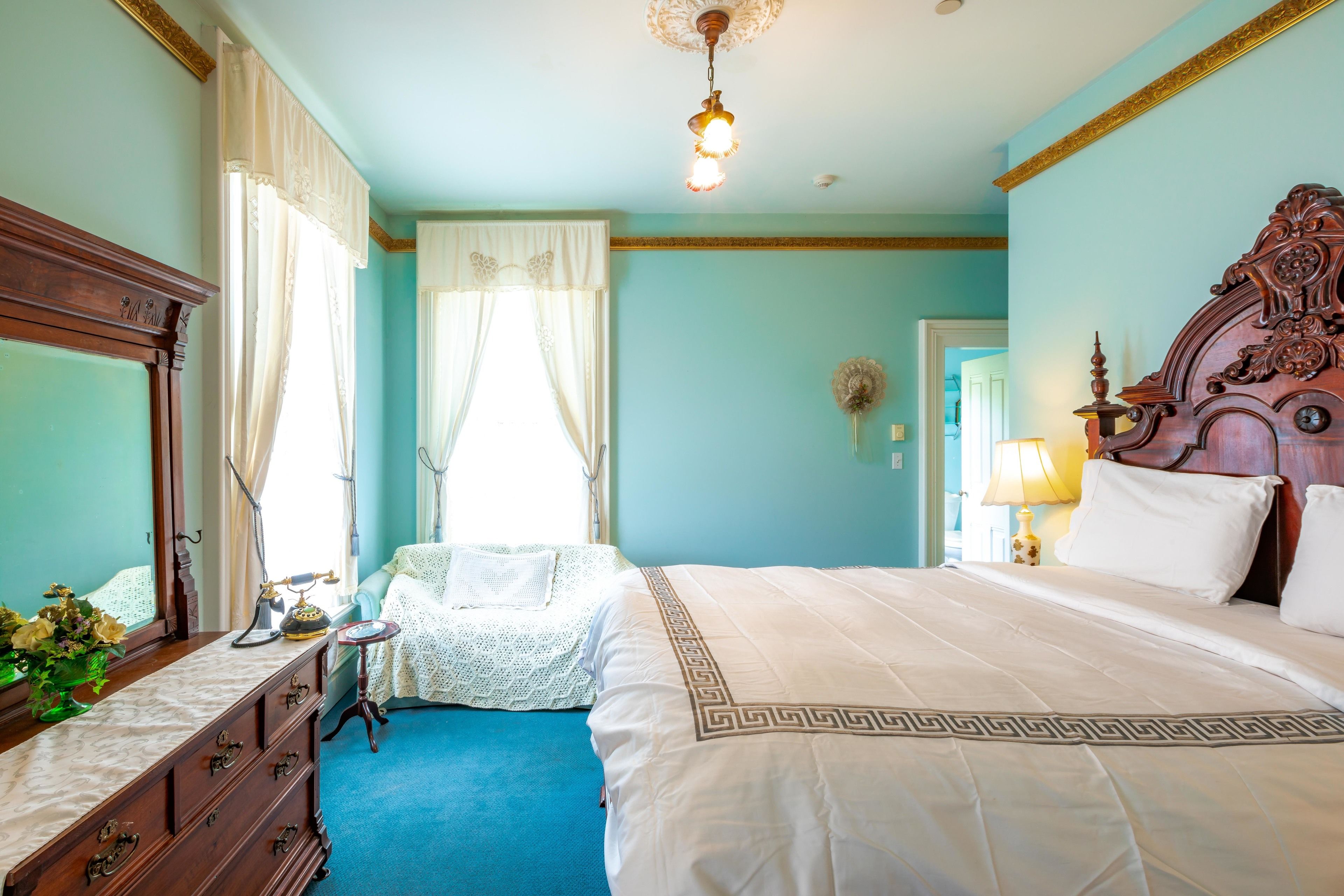 Une chambre à coucher avec un grand lit, une commode, un miroir et une fenêtre avec des rideaux.