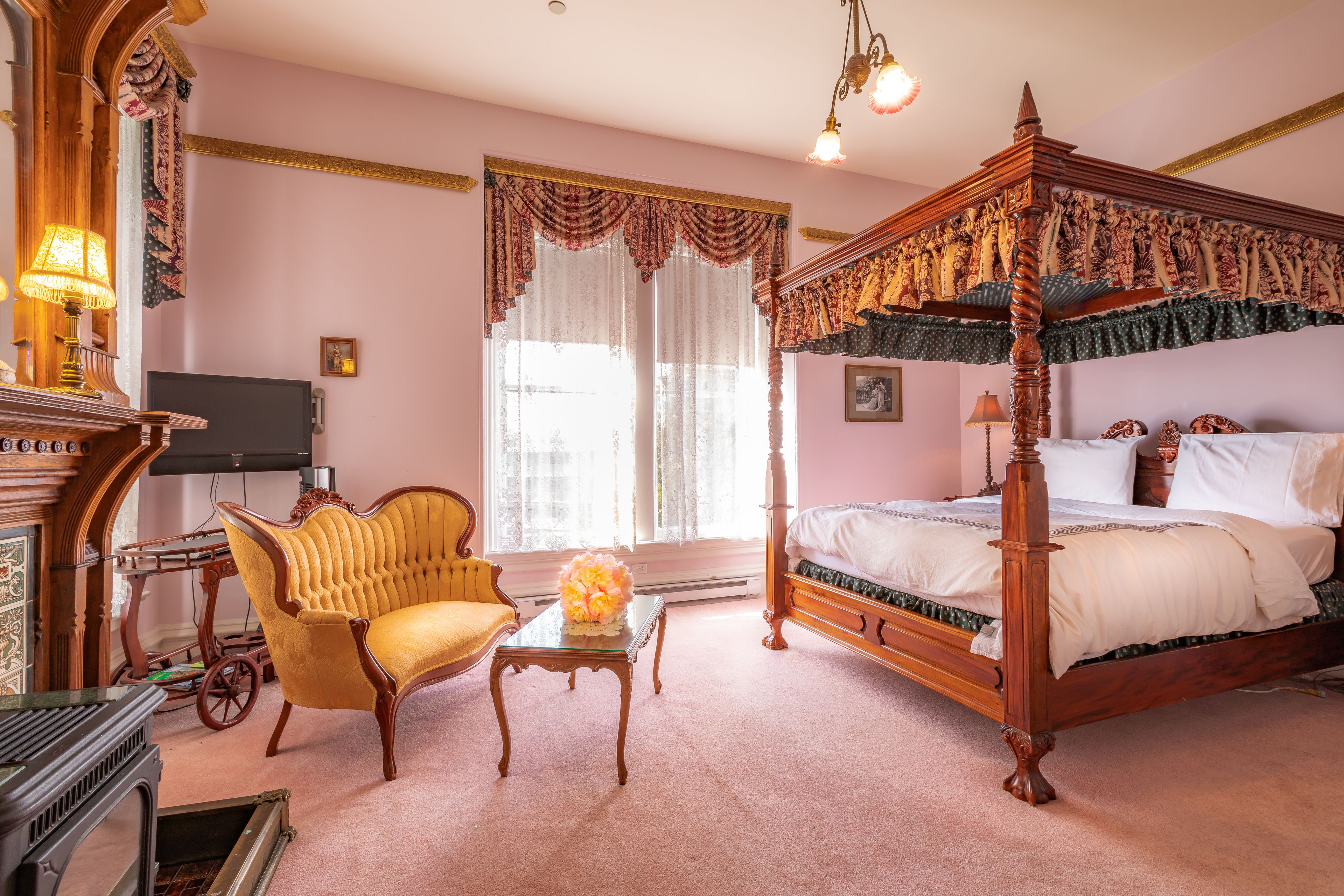 Une chambre à coucher avec un lit à baldaquin, un bureau en bois, un fauteuil jaune et un téléviseur.