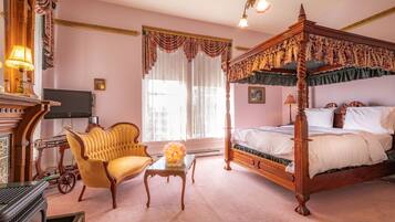A bedroom with a four-poster bed, a wooden desk, a yellow armchair, and a television.