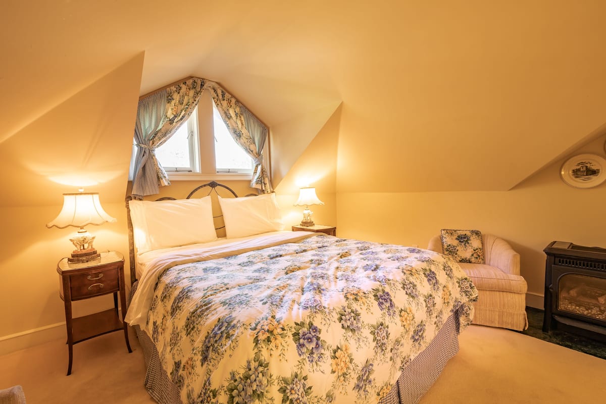 A bedroom with a bed, two bedside tables with lamps, a chair, and a fireplace.