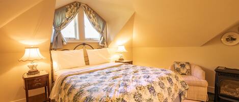 A bedroom with a bed, two bedside tables with lamps, a chair, and a fireplace.