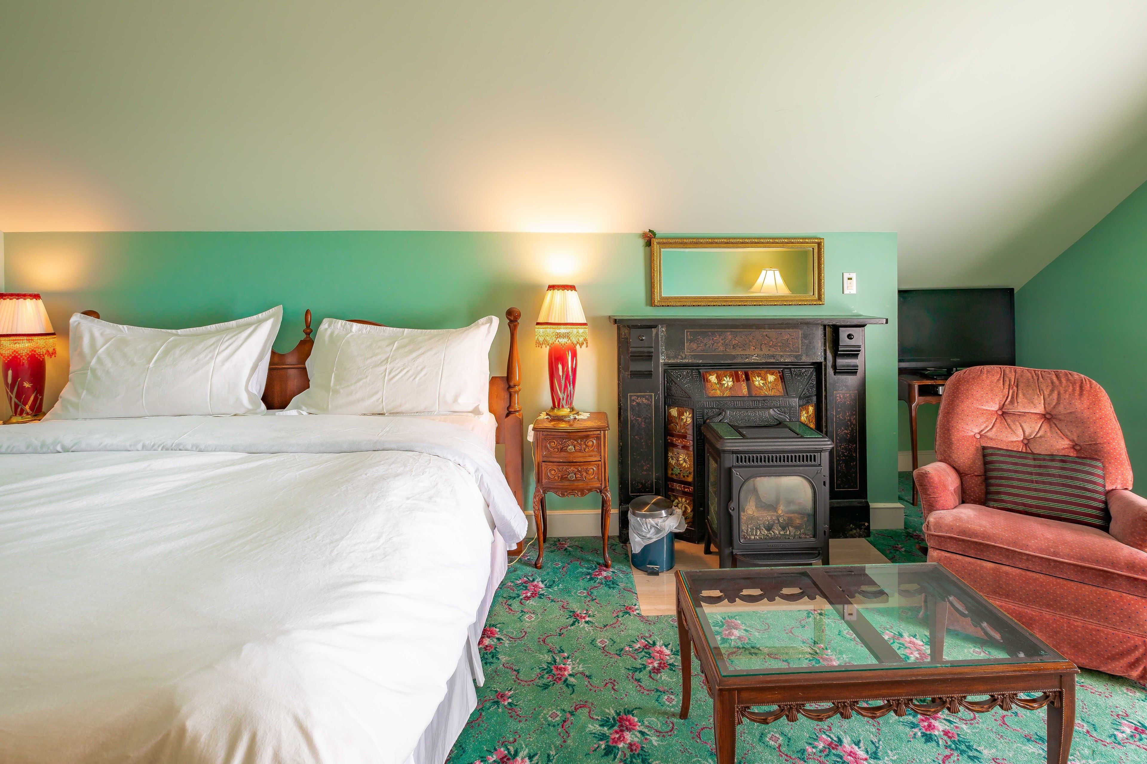 A bedroom with a bed, a fireplace, a chair, and a small table.
