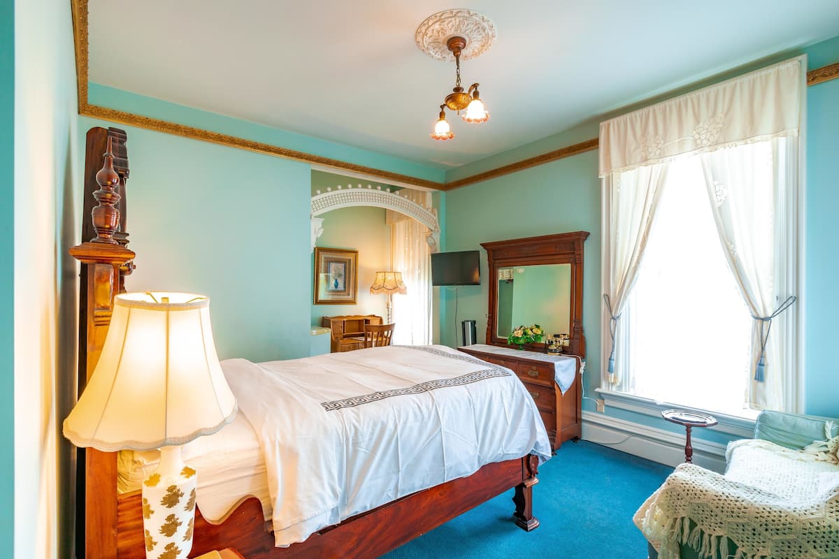 A bedroom with a wooden bed, a desk, a chair, a mirror, and a window with curtains.