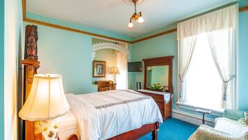 A bedroom with a wooden bed, a desk, a chair, a mirror, and a window with curtains.