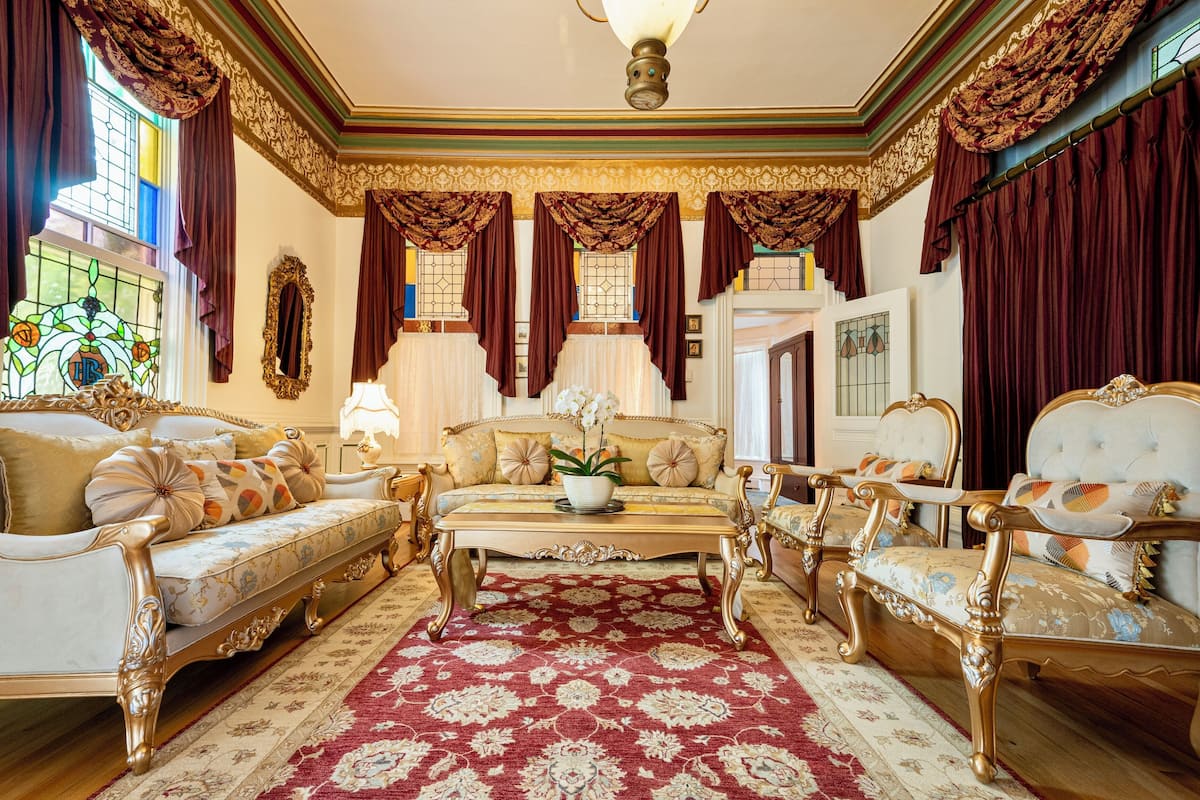 A luxurious room with ornate furniture, a large red patterned rug, and decorative drapery.