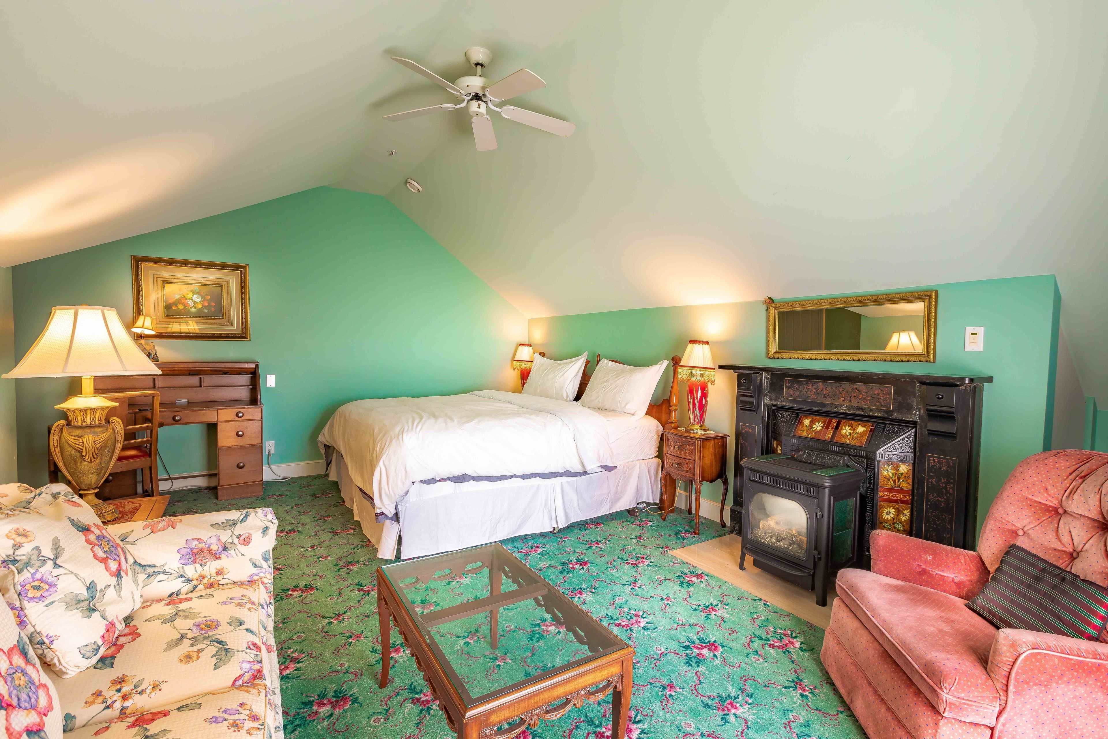 A bedroom with a bed, a desk, a chair, a fireplace, and a ceiling fan.