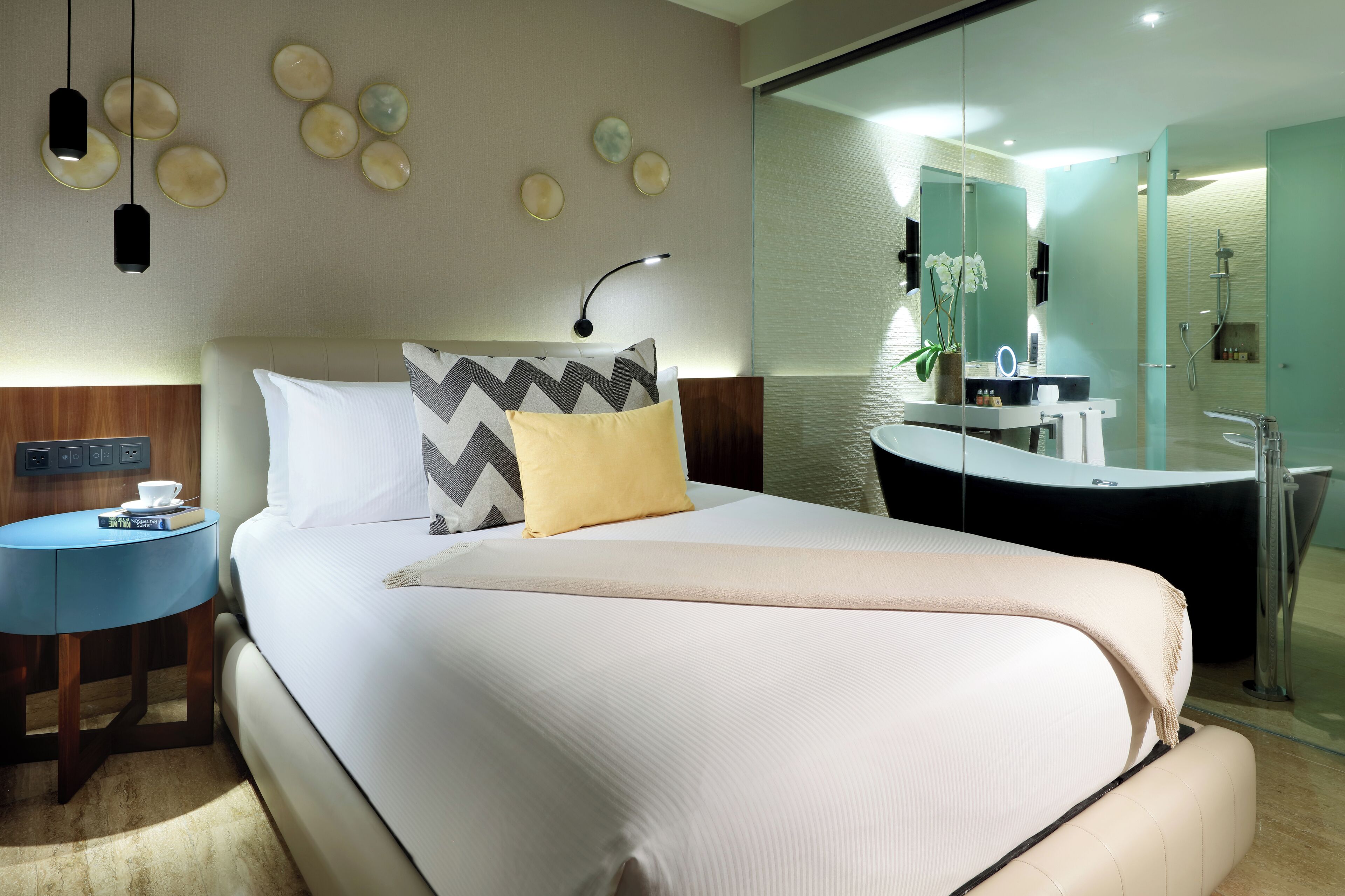 A modern hotel room with a large bed, bedside table, and a bathroom with a bathtub and shower.