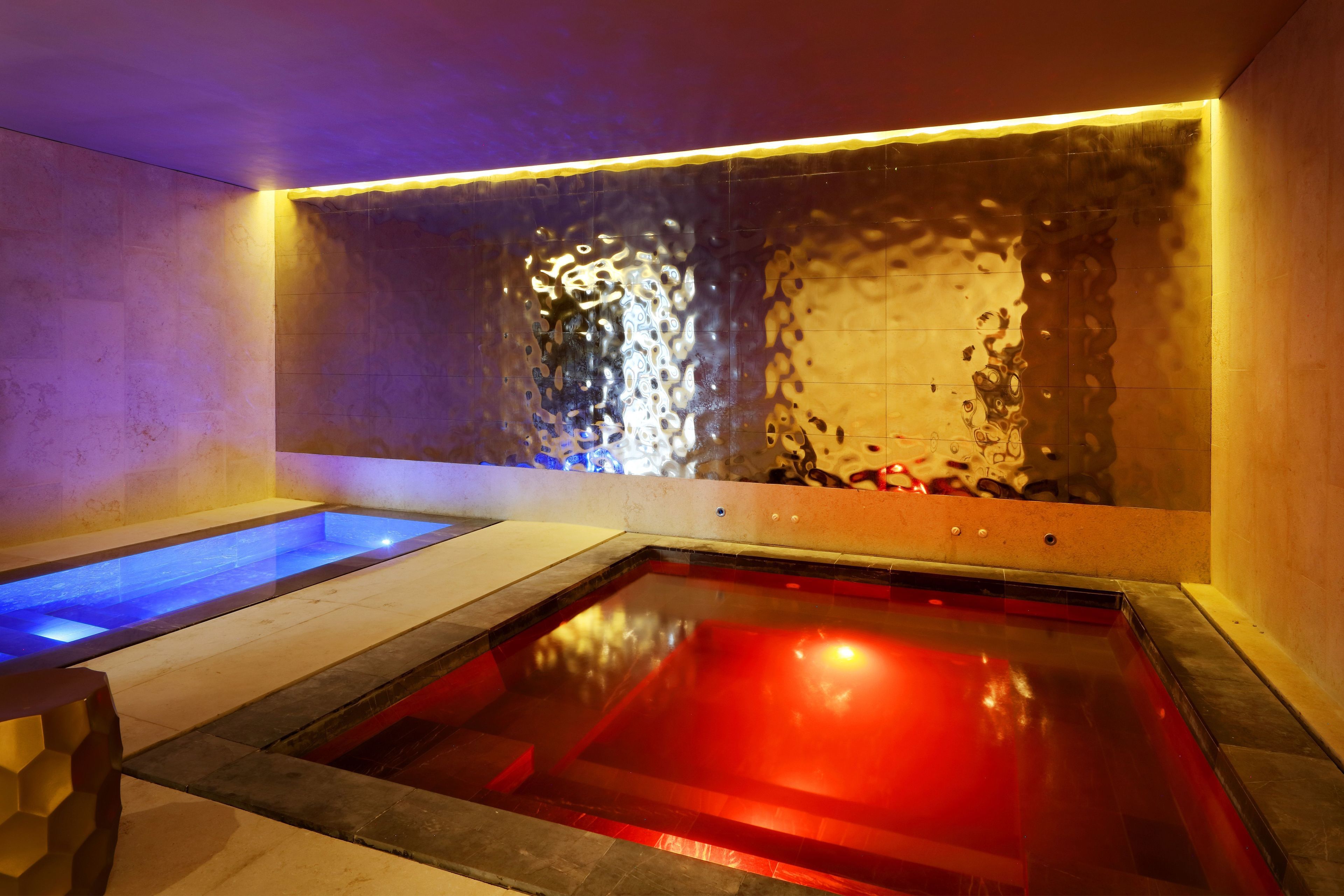A spa area with two separate pools, one with blue lighting and the other with red lighting.