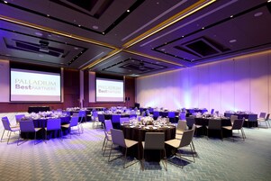 Un salón de conferencias con varias mesas redondas, sillas y una pantalla grande que muestra 'Palladium Best Partners'.